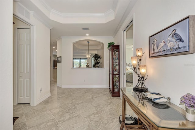 hallway with ornamental molding, a raised ceiling, and light tile floors