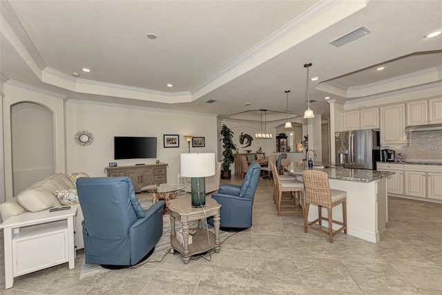 tiled living room with ornamental molding, sink, decorative columns, and a tray ceiling