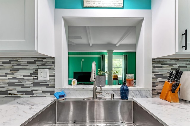 kitchen featuring tasteful backsplash, beam ceiling, white cabinetry, and light stone counters