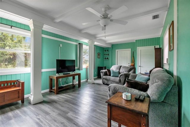 living room featuring wood-type flooring, a wealth of natural light, ornate columns, and beamed ceiling