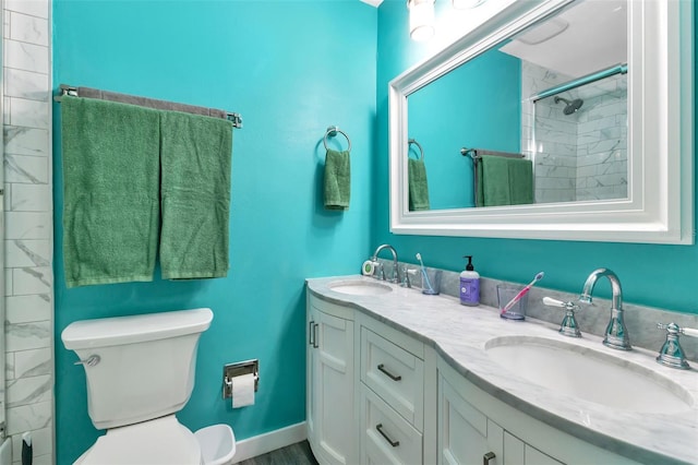 bathroom with a tile shower, toilet, and dual bowl vanity