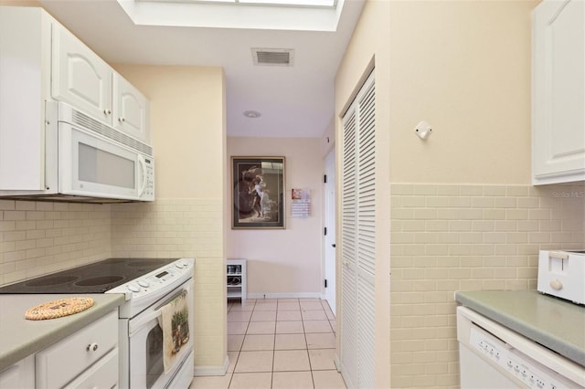 kitchen featuring a skylight, light tile floors, white appliances, backsplash, and white cabinetry