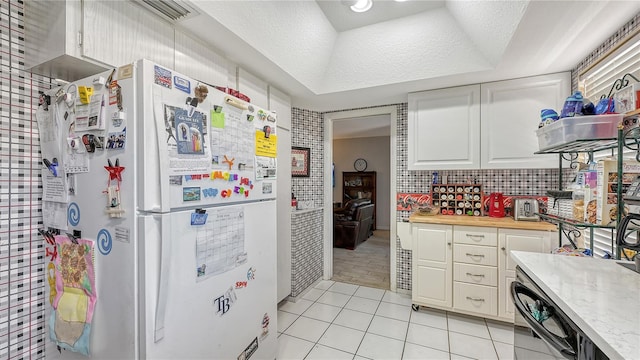 kitchen featuring white refrigerator, white cabinets, and light tile floors