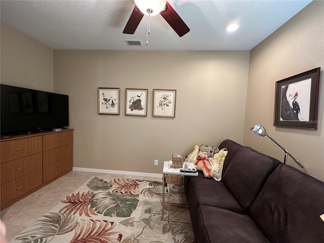 living room with ceiling fan, light tile floors, and a textured ceiling