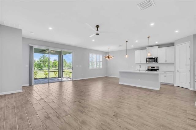 unfurnished living room featuring ceiling fan with notable chandelier and sink