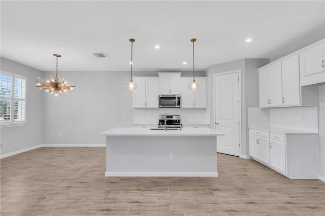 kitchen with white cabinets, appliances with stainless steel finishes, a kitchen island with sink, and pendant lighting