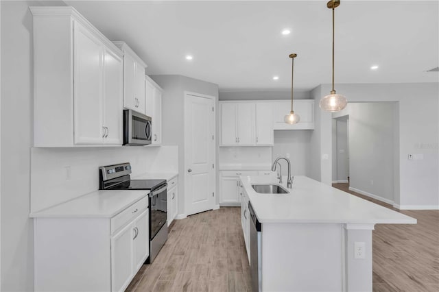 kitchen with white cabinets, appliances with stainless steel finishes, a center island with sink, and sink