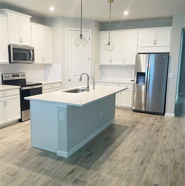 kitchen featuring stainless steel appliances, sink, decorative light fixtures, white cabinets, and an island with sink