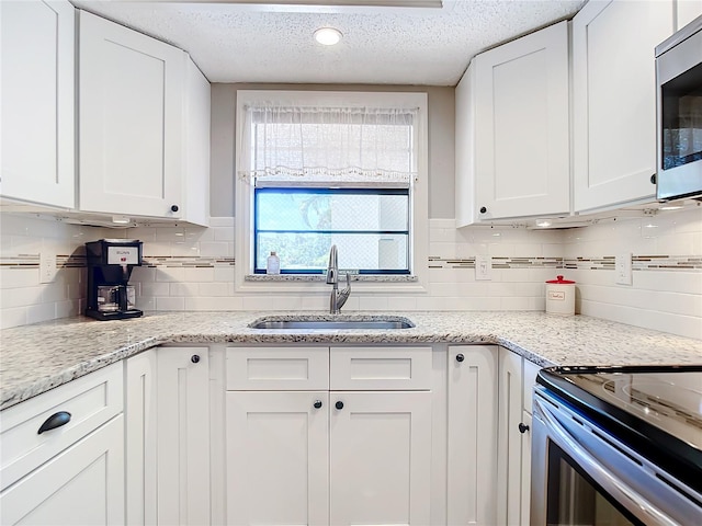 kitchen featuring appliances with stainless steel finishes, a textured ceiling, sink, backsplash, and white cabinetry