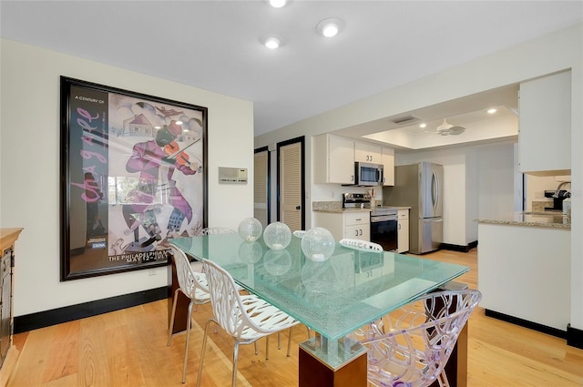 dining area with sink, a raised ceiling, and light wood-type flooring