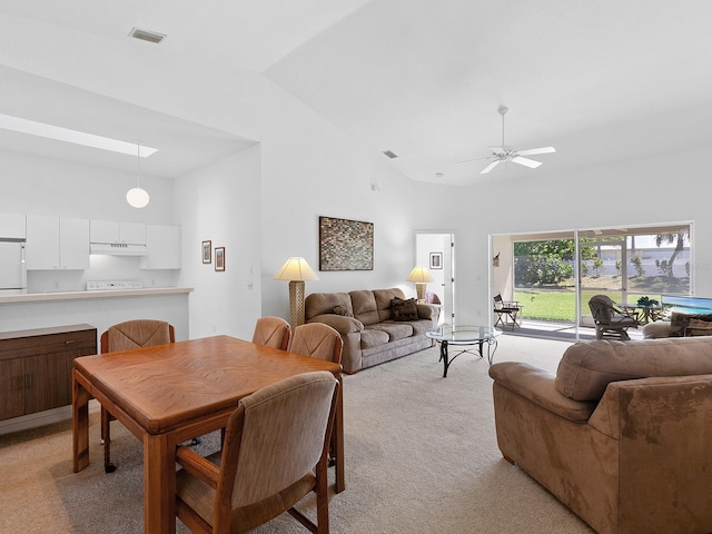 dining room with ceiling fan, light colored carpet, a skylight, and high vaulted ceiling