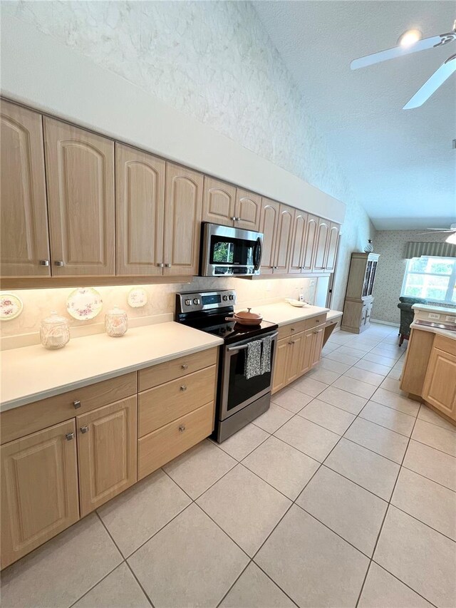 kitchen with appliances with stainless steel finishes, light brown cabinetry, a textured ceiling, light tile patterned floors, and lofted ceiling