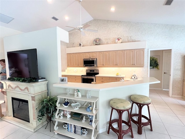 kitchen with light brown cabinets, a kitchen breakfast bar, appliances with stainless steel finishes, light tile patterned flooring, and kitchen peninsula