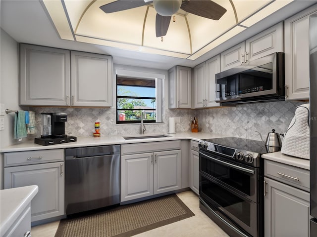 kitchen featuring stainless steel appliances, decorative backsplash, sink, gray cabinets, and ceiling fan