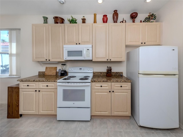 kitchen featuring dark stone countertops, light brown cabinetry, white appliances, and light tile flooring