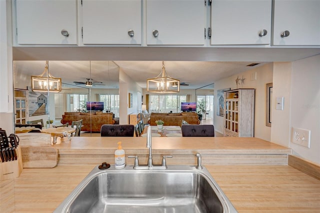 kitchen featuring white cabinetry, decorative light fixtures, ceiling fan with notable chandelier, and sink