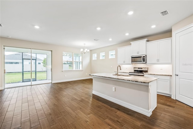 kitchen featuring a center island with sink, light stone counters, white cabinetry, stainless steel appliances, and a chandelier