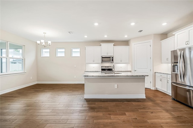 kitchen with light stone countertops, a kitchen island with sink, white cabinets, and stainless steel appliances