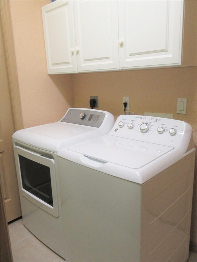 laundry room with electric dryer hookup, cabinets, light tile floors, and washer and dryer