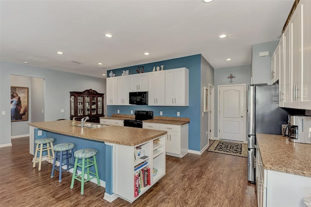 kitchen with white cabinets, black appliances, hardwood / wood-style floors, sink, and a center island with sink