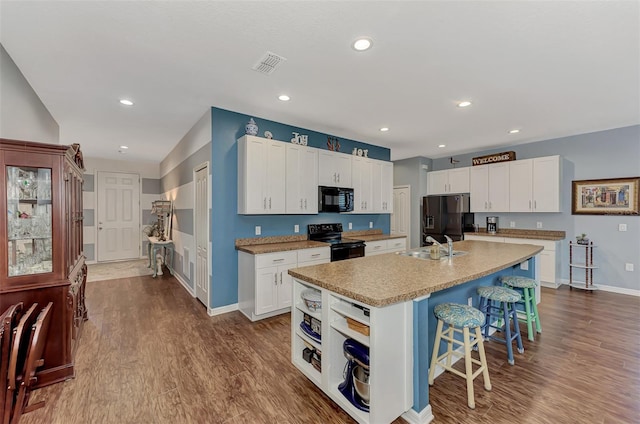 kitchen featuring white cabinets, hardwood / wood-style flooring, a kitchen island with sink, and black appliances