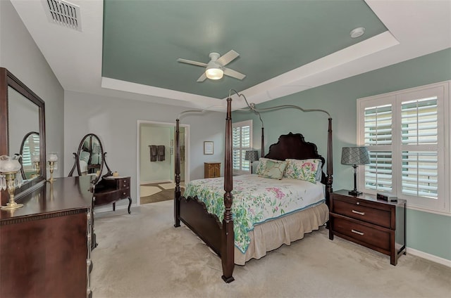 carpeted bedroom with a raised ceiling, ceiling fan, and multiple windows