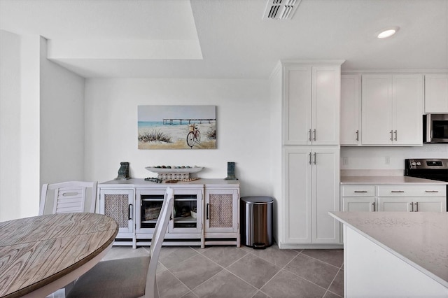 kitchen with stainless steel appliances, light stone counters, white cabinetry, and light tile floors