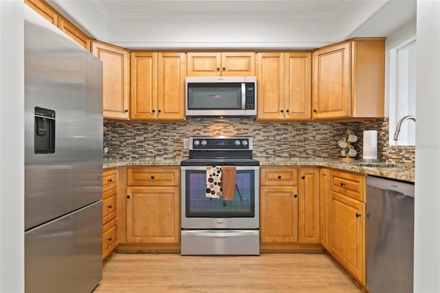 kitchen featuring stainless steel appliances, light hardwood / wood-style flooring, light stone counters, and backsplash