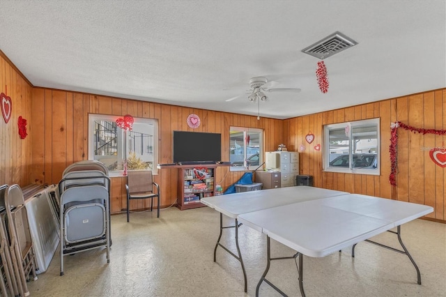 recreation room featuring plenty of natural light, ceiling fan, and wooden walls