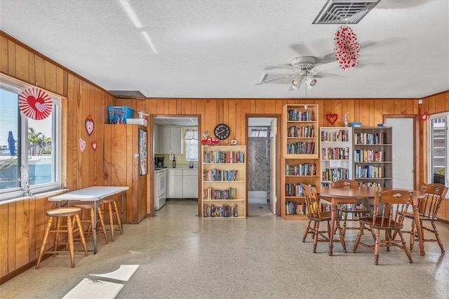 dining area featuring wooden walls, ceiling fan, and a textured ceiling