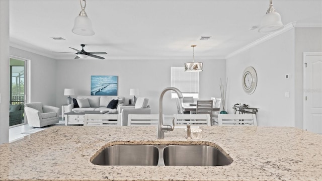 kitchen featuring ornamental molding, ceiling fan with notable chandelier, light stone counters, decorative light fixtures, and sink