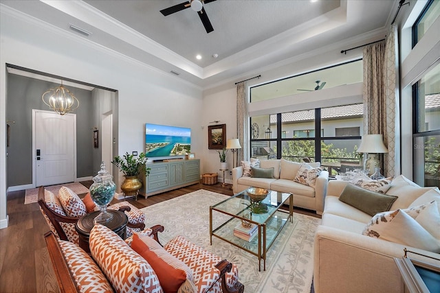 living room featuring crown molding, a tray ceiling, ceiling fan with notable chandelier, and hardwood / wood-style flooring