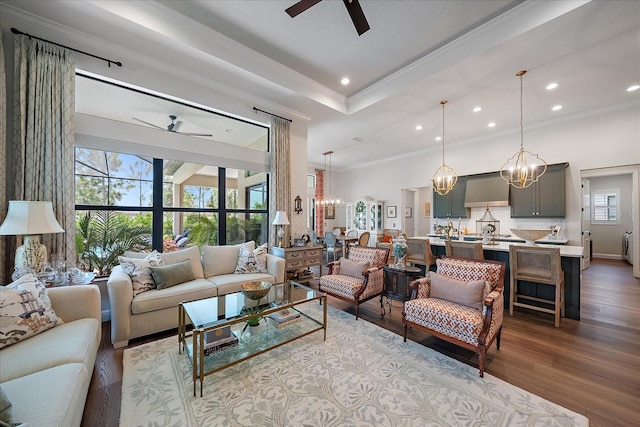 living room with ornamental molding, a raised ceiling, ceiling fan with notable chandelier, and light hardwood / wood-style flooring