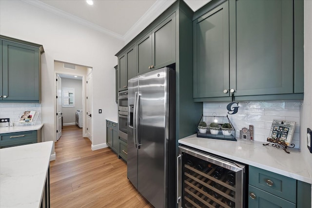 kitchen with washing machine and clothes dryer, light stone counters, stainless steel fridge with ice dispenser, ornamental molding, and beverage cooler