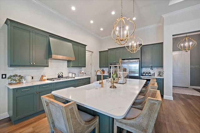 kitchen with premium range hood, sink, decorative light fixtures, appliances with stainless steel finishes, and an island with sink