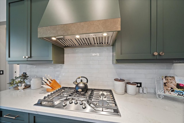 kitchen with light stone counters, stainless steel gas cooktop, green cabinetry, and premium range hood