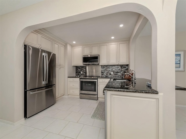 kitchen with appliances with stainless steel finishes, tasteful backsplash, sink, dark stone countertops, and light tile patterned flooring