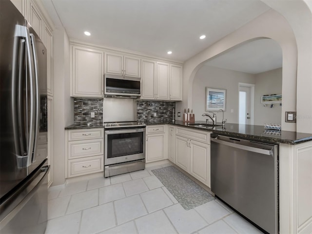 kitchen with sink, stainless steel appliances, kitchen peninsula, dark stone counters, and decorative backsplash