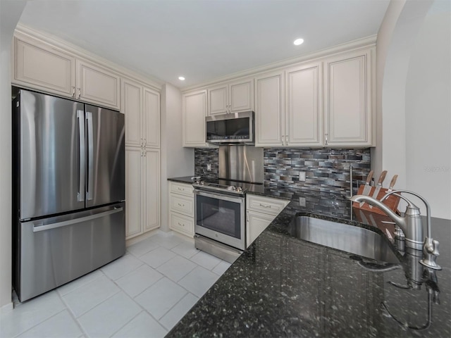 kitchen featuring dark stone counters, cream cabinetry, decorative backsplash, light tile patterned floors, and appliances with stainless steel finishes