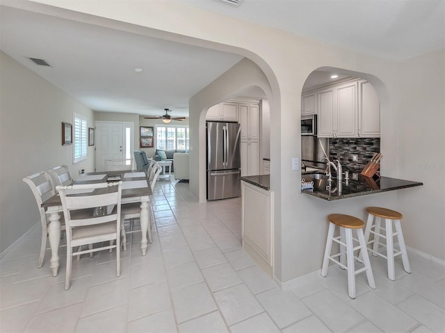 kitchen with backsplash, ceiling fan, light tile patterned floors, appliances with stainless steel finishes, and kitchen peninsula