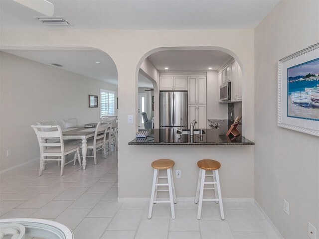 kitchen with white cabinetry, stainless steel appliances, kitchen peninsula, dark stone counters, and a breakfast bar area