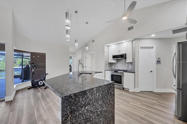 kitchen with white cabinets, appliances with stainless steel finishes, decorative light fixtures, an island with sink, and sink