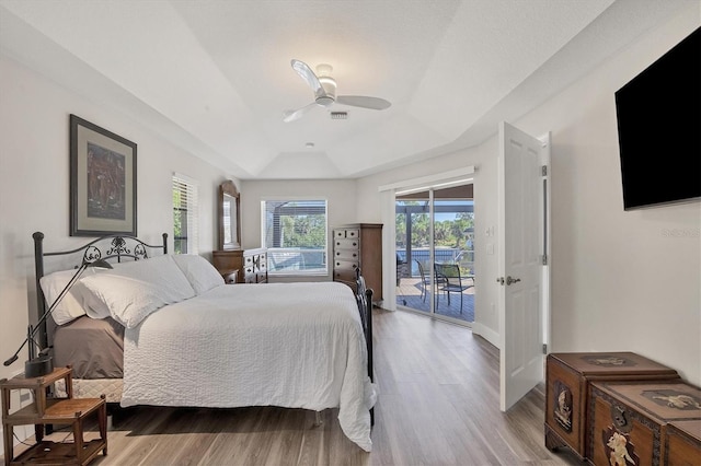 bedroom with access to outside, light wood-type flooring, ceiling fan, and a raised ceiling