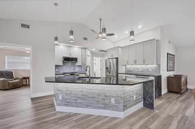 kitchen with pendant lighting, stainless steel appliances, dark stone counters, sink, and a center island with sink