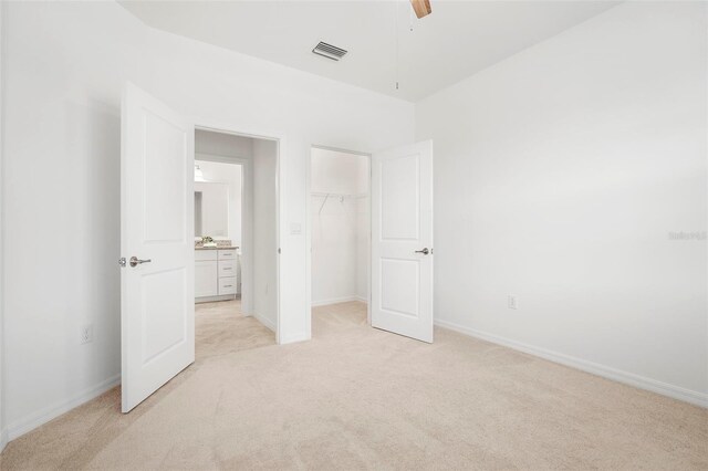 unfurnished bedroom with light carpet, a walk in closet, ceiling fan, and a closet