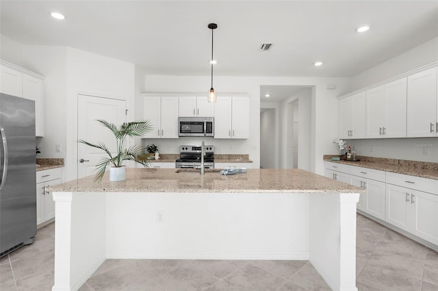 kitchen with appliances with stainless steel finishes, light stone counters, a center island with sink, and hanging light fixtures