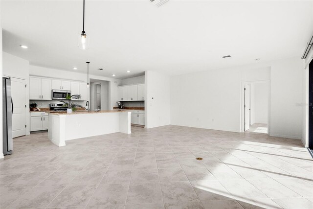 kitchen featuring white cabinets, decorative light fixtures, stainless steel appliances, sink, and a center island with sink