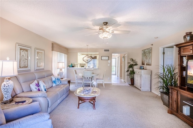 carpeted living room with ceiling fan with notable chandelier and a textured ceiling