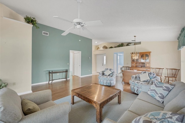 living room featuring ceiling fan with notable chandelier, vaulted ceiling, and light hardwood / wood-style flooring