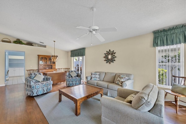 living room featuring hardwood / wood-style floors, ceiling fan with notable chandelier, lofted ceiling, and a textured ceiling